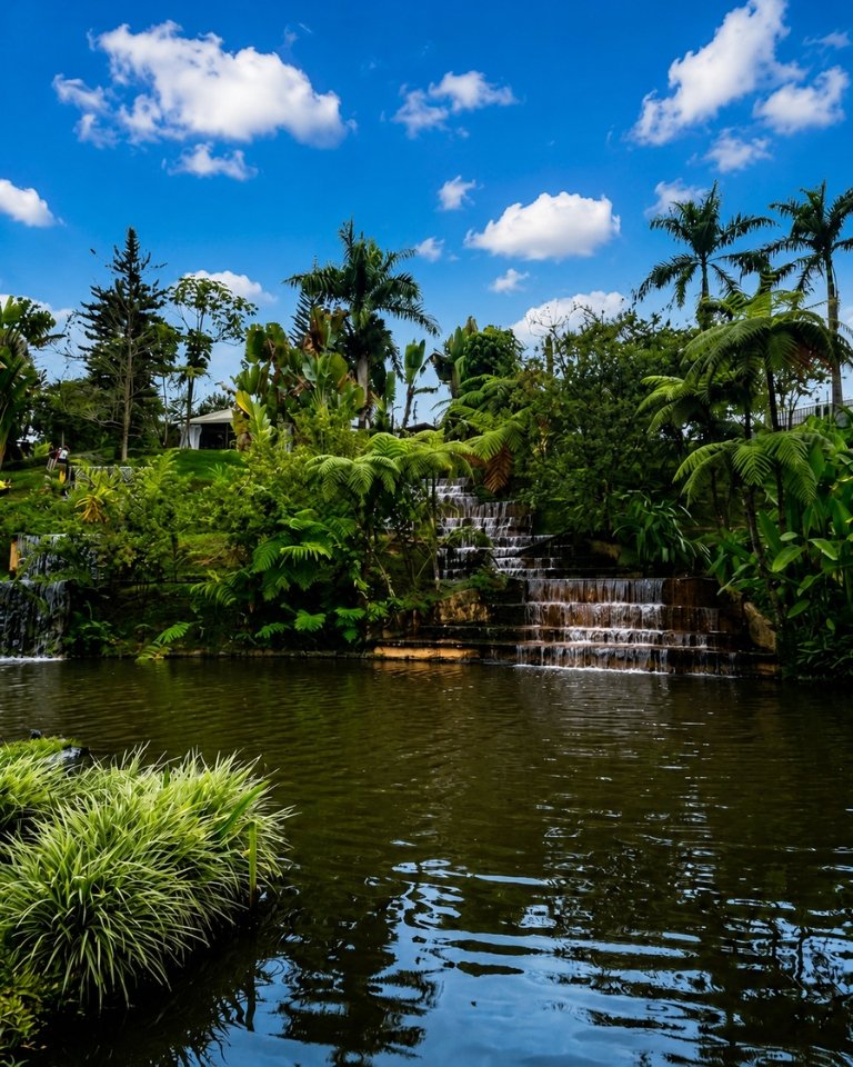 Cascada artificial escalonada rodeada de palmeras, plantas tropicales y un lago en el Parque de la Vida de Armenia, Quindío.