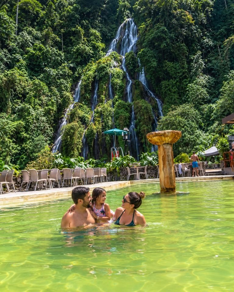 amilia con una niña disfrutando de una piscina de agua termal con la cascada y el bosque al fondo en Santa Rosa de Cabal